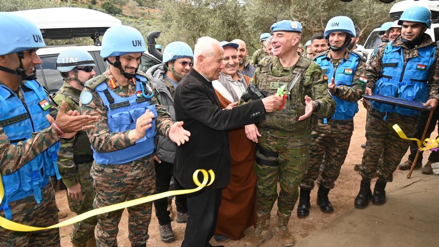 A man cuts a yellow ribbon as peacekeepers in uniform watch on and applaud.