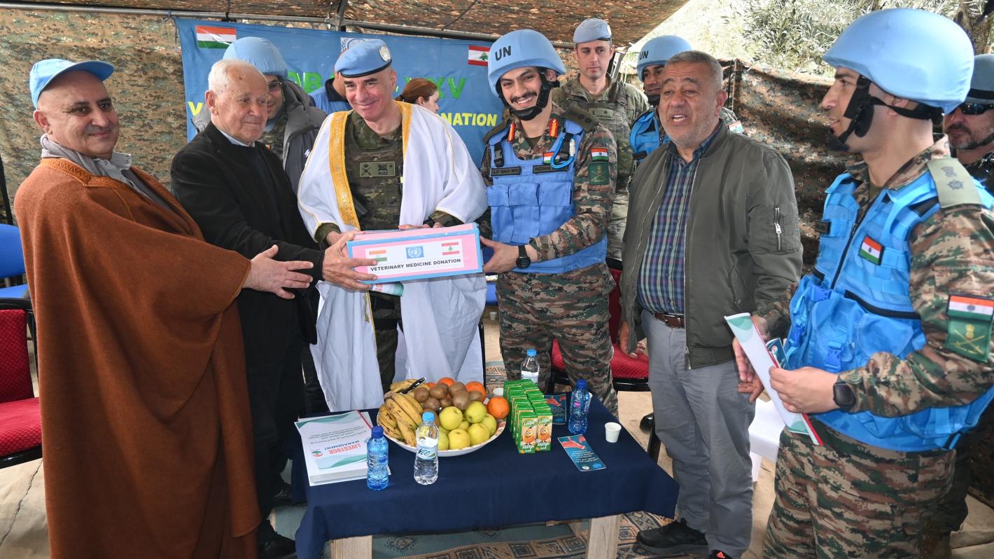 A group of peacekeepers and civilians standing around a table where food is served.