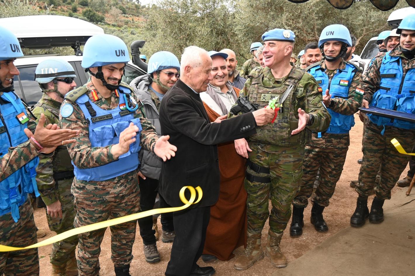 A man cuts a yellow ribbon as peacekeepers in uniform watch on and applaud.